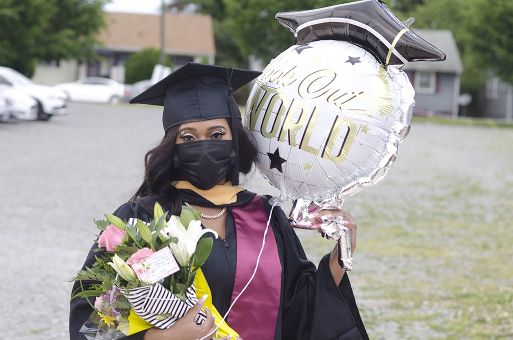 A B-S-W graduate, masked, carrying a bouquet of flowers and a balloon