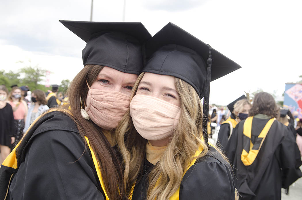 Two B-S-W graduates, a mother and daughter, celebrate with a hug. Both wear masks.