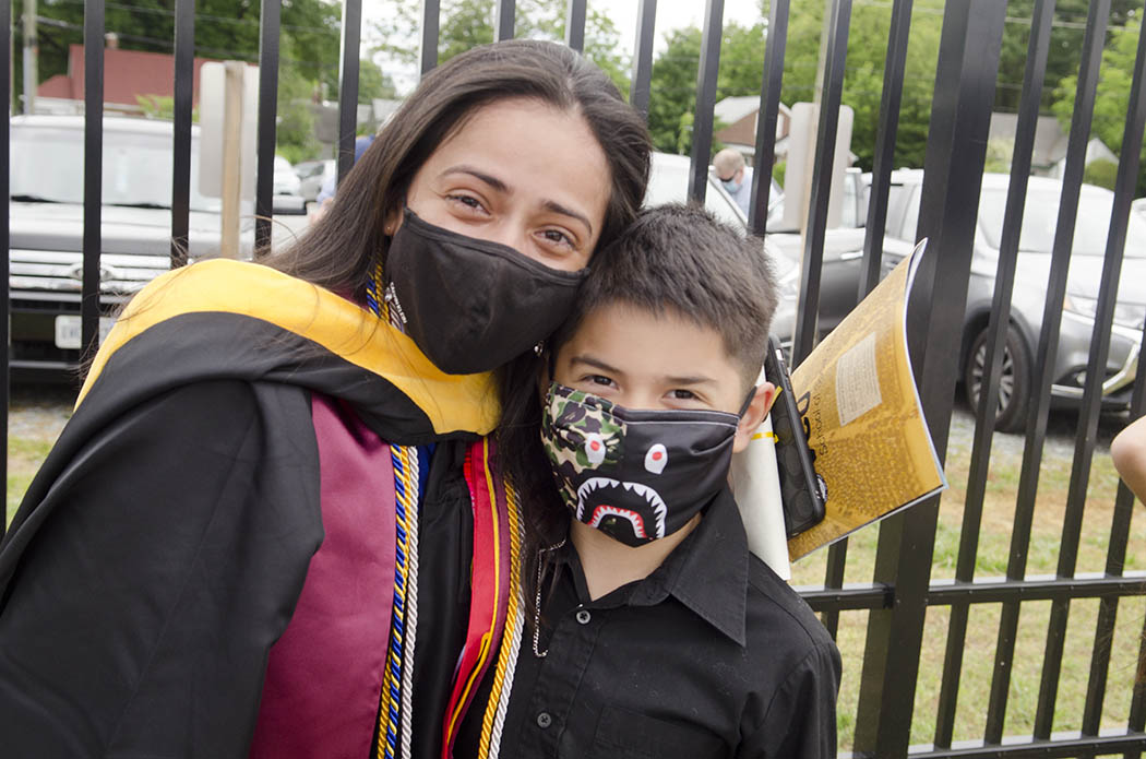 A B-S-W graduate celebrates with a young guest. Both wear masks.