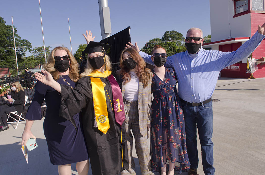 An M-S-W graduate and four guests hold their arms out in celebration. All are wearing masks.