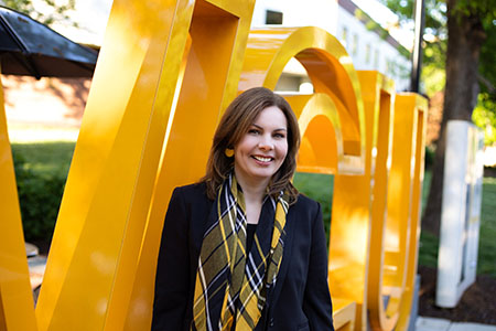Interim Dean Rebecca Gomez stands in front of a gold VCU sign on the Monroe Park Campus
