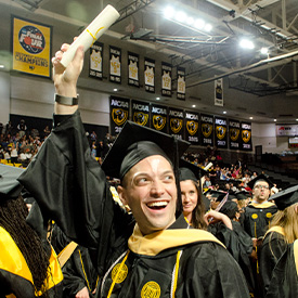 A social work graduate holds their scroll over their head in celebration at the May Commencement ceremony
