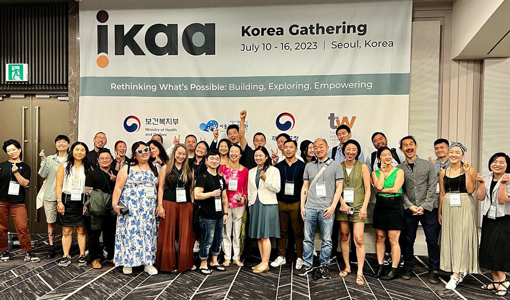 Assistant Professor Hollee McGinnis, Ph.D., poses with colleagues at the International Korean Adoptee Associations Korea Gathering. A sign behind the group says IKAA, July 10-16, 2023, Seoul, South Korea. Rethinking what is possible: Building, exploring, empowering.
