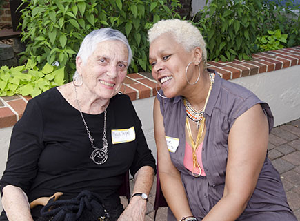 Flossie Segal, in a black blouse, smiles as she sits next to Gayle Harris, wearing a pink blouse with mauve sleeveless top.