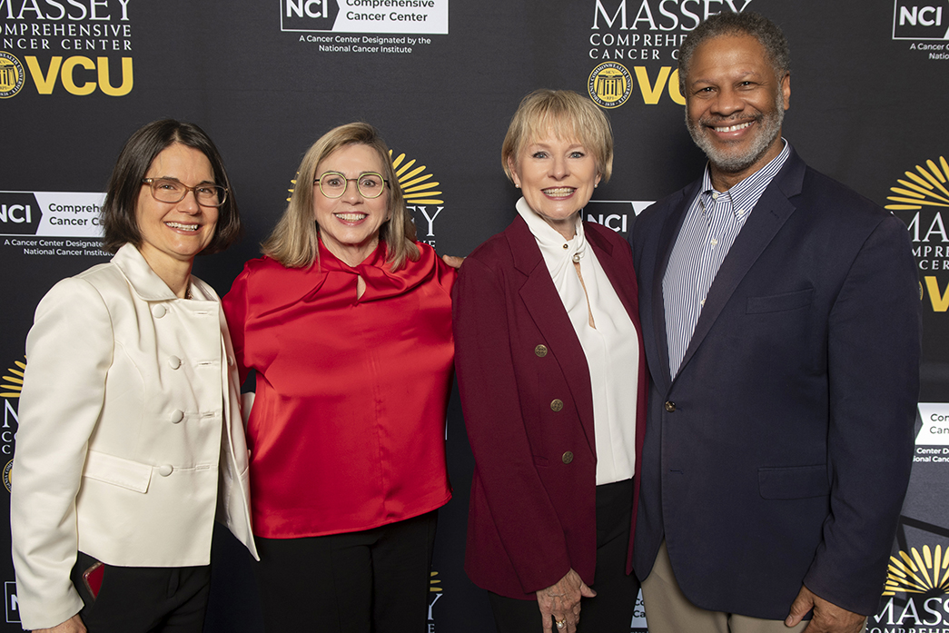 Four people stand smiling in front of a backdrop that reads Massey Comprehensive Cancer Center-VCU.